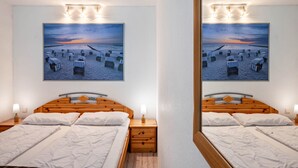 A hotel room with a wooden bed, two bedside tables, a nightstand, a large framed picture of a beach, and a mirror.