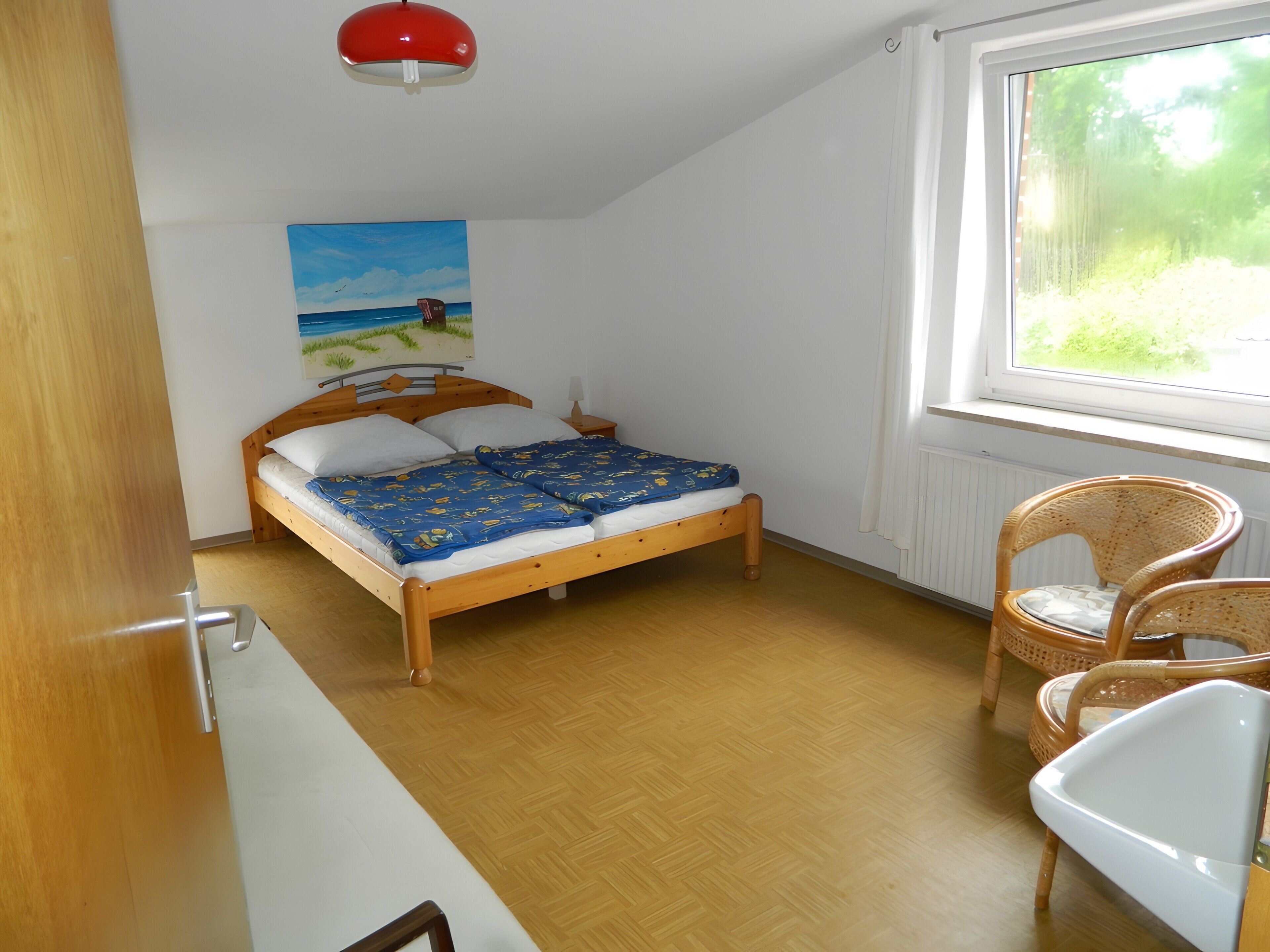 A bedroom with a wooden bed, a painting on the wall, a window with a view, and a chair.