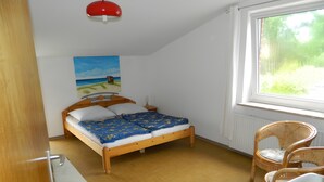 Een slaapkamer met een houten bed, een schilderij aan de muur, een raam met uitzicht en een stoel.