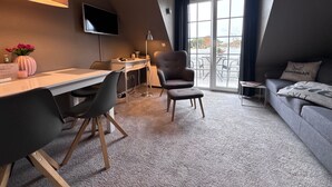 Una habitación moderna con escritorio, sillas, sofá, televisor y un ventanal con cortinas.
