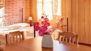 A wooden dining table with a white vase containing pink flowers.