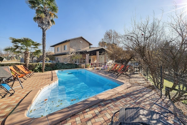 Une piscine avec des chaises longues, une maison et un palmier.
