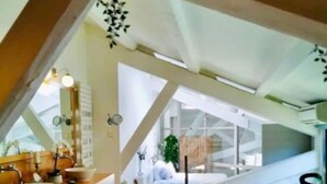 Een moderne badkamer met een houten wastafel, een ruim bad en uitzicht op een slaapkamer door een dakraam.