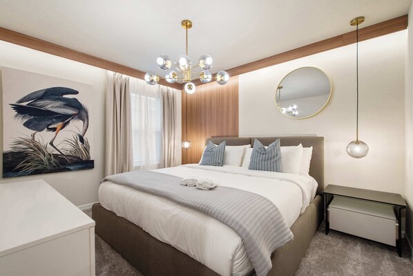 A modern bedroom with a large bed, a bedside table, a nightstand, a mirror, and a chandelier.