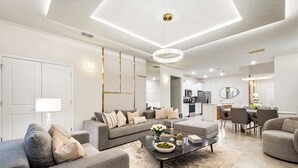 A modern living room with a sofa, coffee table, and dining area. - Family Fun Villa: Themes, Pool & Games,Resort (Clermont)
