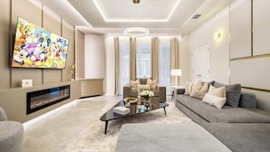 A modern living room with a flat-screen TV, a fireplace, a sofa, and a coffee table. - Family Fun Villa: Themes, Pool & Games,Resort (Clermont)