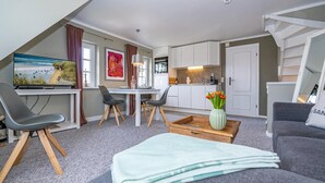 A modern living room with a TV, seating, a dining area, and a kitchen. - Apartment 'Gemütliche Wohnung' with Shared Garden and Wi-Fi (Keitum)
