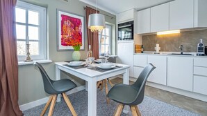 A modern kitchen with white cabinets, a dining table with chairs, a pendant light, and a window with curtains. - Apartment 'Gemütliche Wohnung' with Shared Garden and Wi-Fi (Keitum)