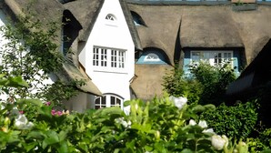 A building with a unique thatched roof and white walls, surrounded by greenery. - Apartment 'Gemütliche Wohnung' with Shared Garden and Wi-Fi (Keitum)