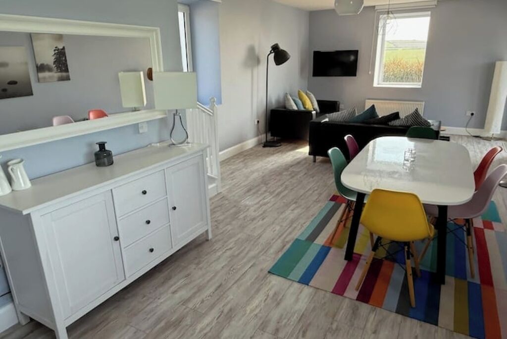 A modern living room with a white sofa, a dining table with colorful chairs, a white cabinet, and a floor lamp.