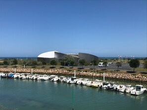 A marina with boats docked, a modern building with a curved roof, and a clear blue sky. - Le petit large, stunning views, close to the beach and all amenities (Courseulles-sur-Mer)