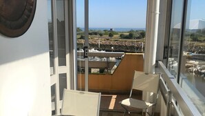 Een balkon met een ronde tafel en twee stoelen, uitzicht op zee en een stenen muur op de achtergrond.