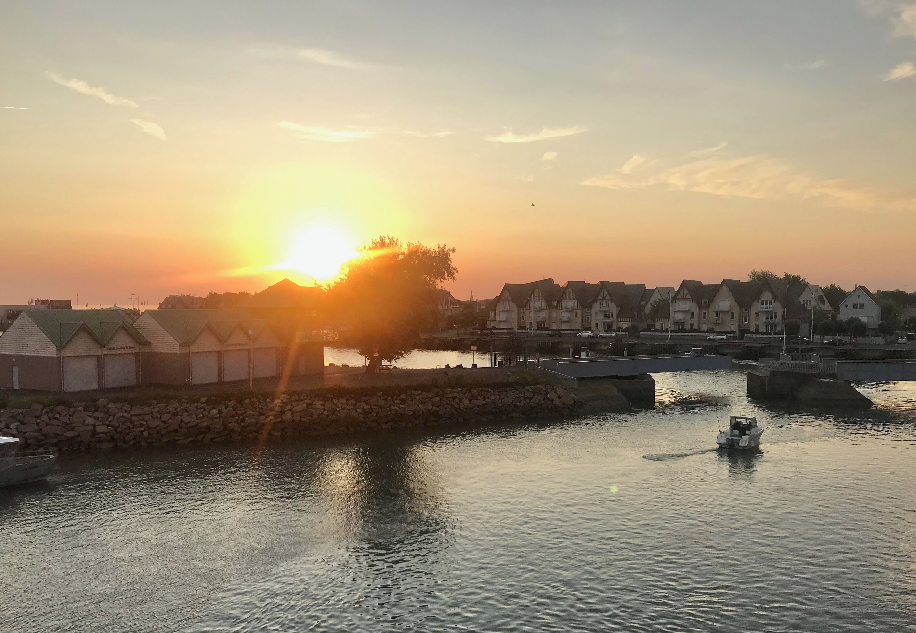 A sunset over a waterfront with traditional houses and a small boat on the water.