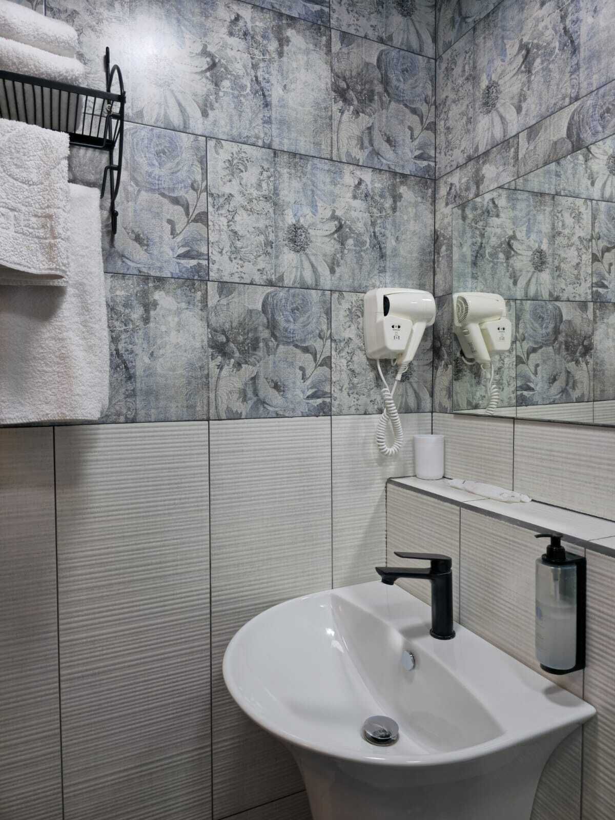A bathroom with a white sink, a towel rack, and two hair dryers mounted on the wall.