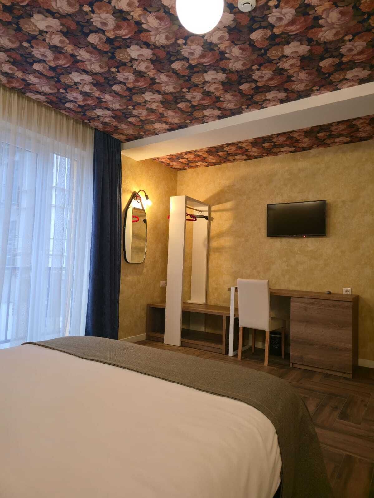 A hotel room with a bed, a desk, a chair, a television, and a mirror.