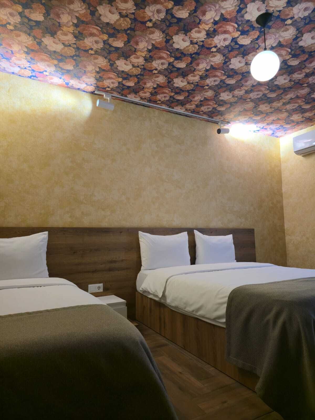 Une chambre d’hôtel avec deux lits, des têtes de lit en bois et un plafond orné de motifs floraux.