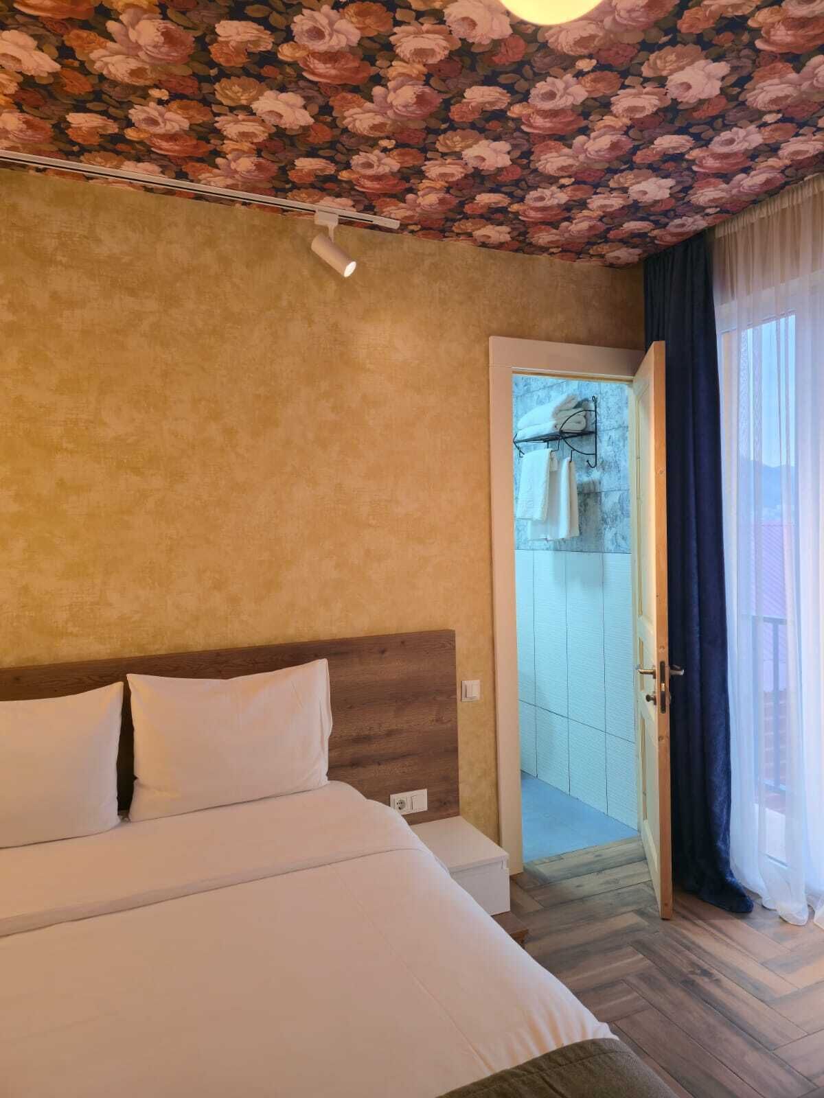A bedroom with a bed, a wooden headboard, a floral ceiling, and a view of a balcony.