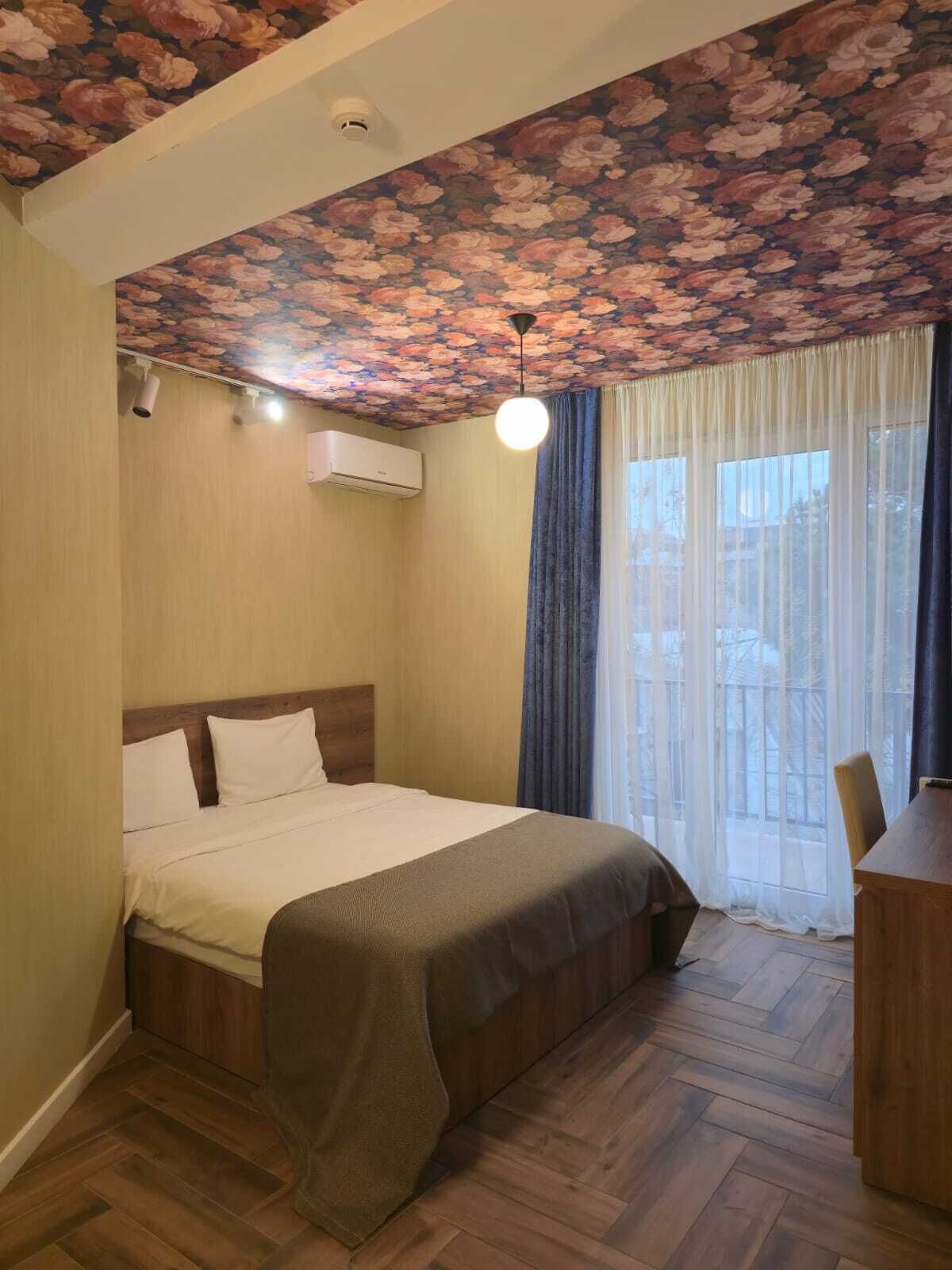 A bedroom with a floral ceiling, a bed with white bedding, a wooden headboard, and a window with curtains.
