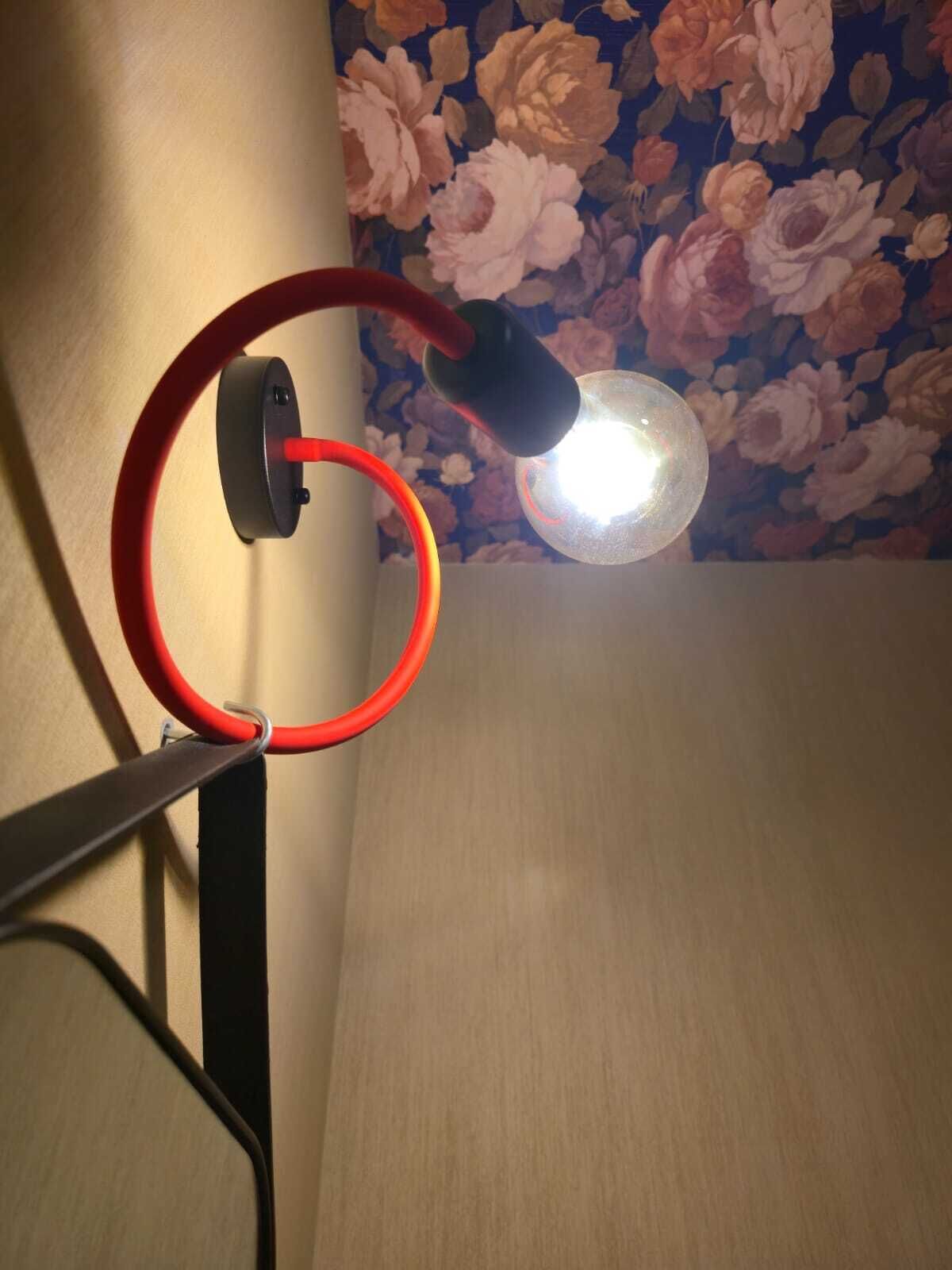 Un coin de pièce avec un papier peint à motifs floraux, un plancher en bois et un luminaire fixé au mur.