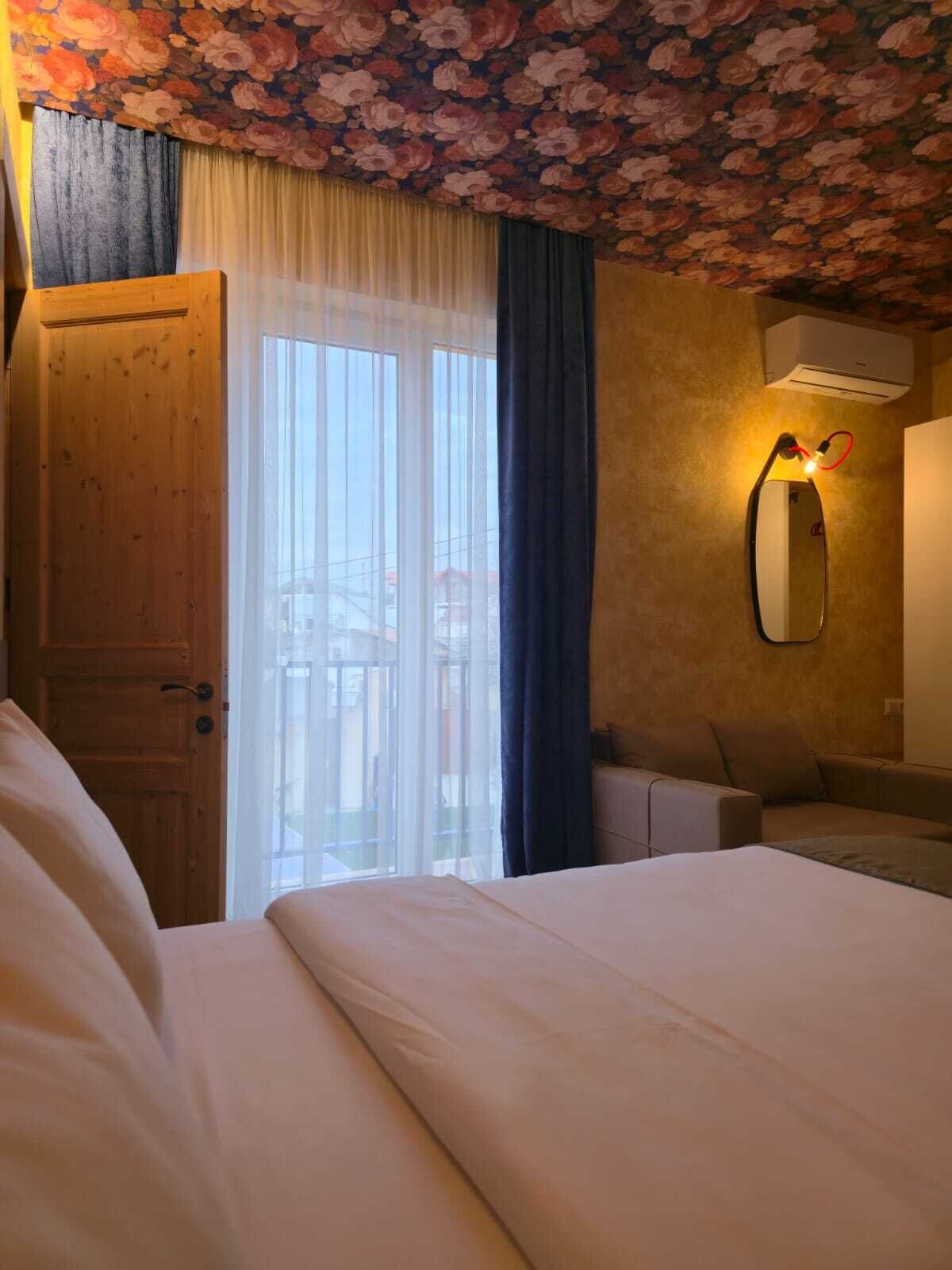A hotel room with a wooden door, a bed, a desk, and a mirror.