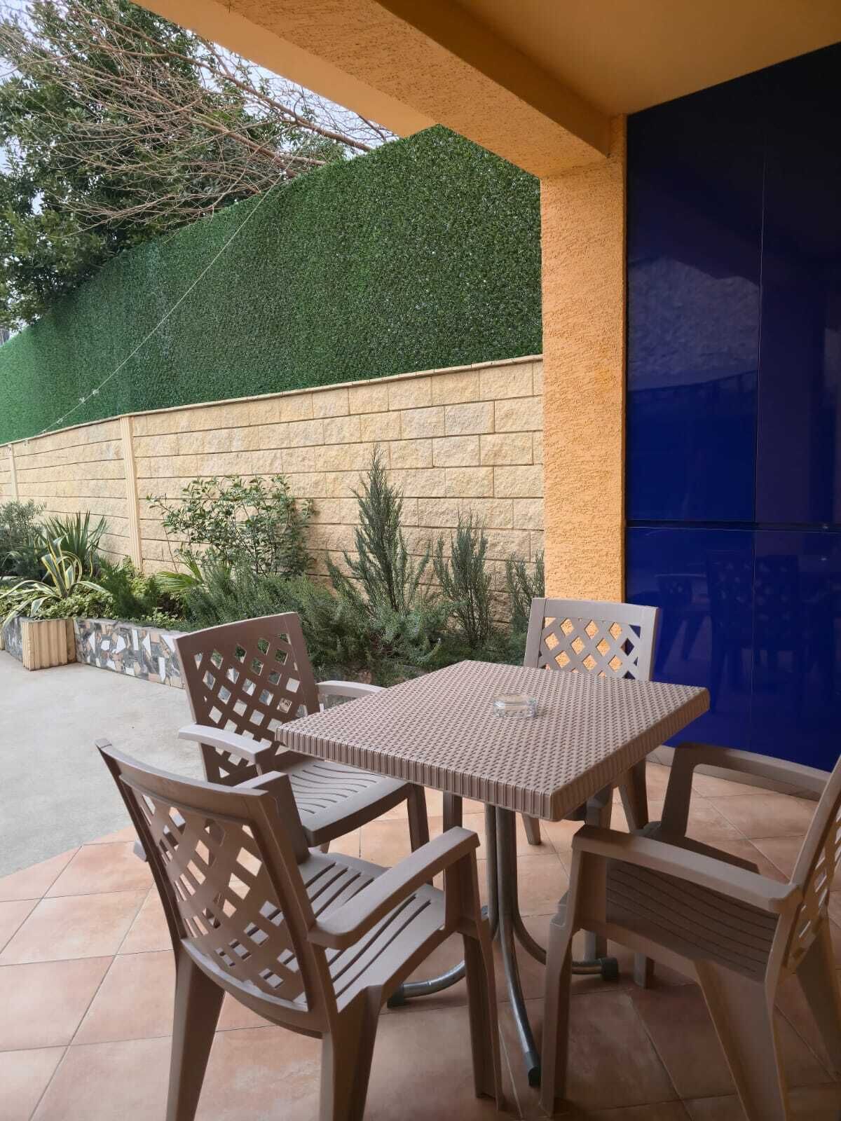 An outdoor patio with a table and chairs, surrounded by a stone wall and greenery.