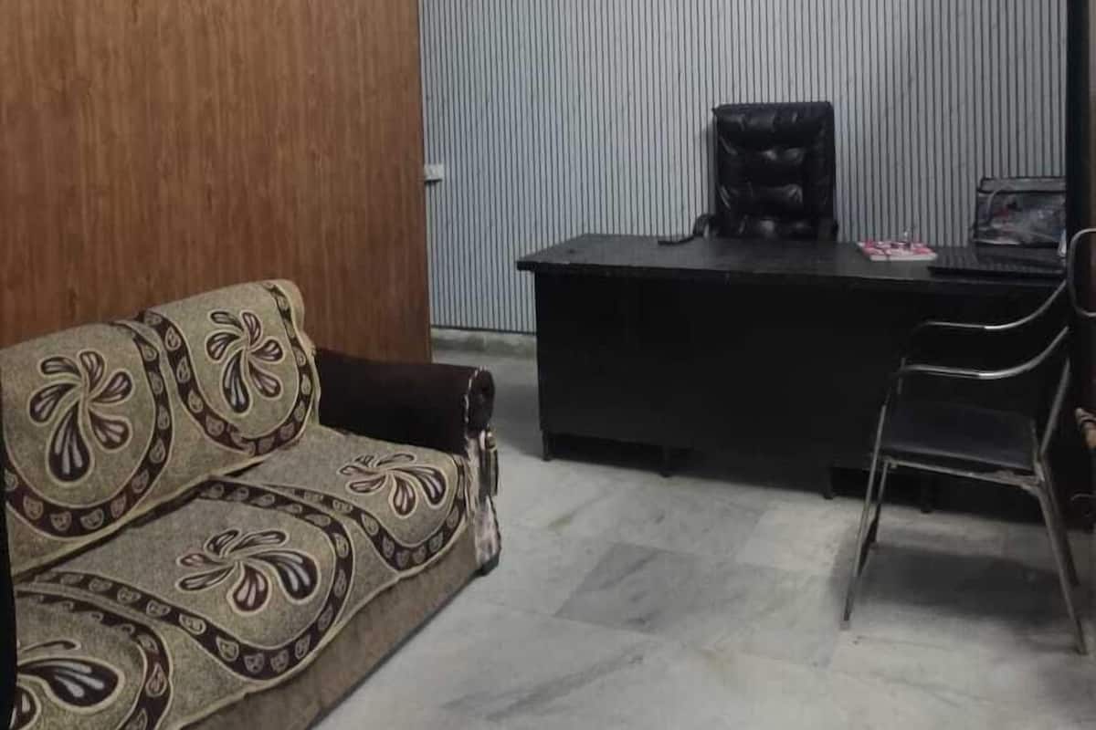 A room with a wooden wall, a sofa with a floral pattern, a desk with a chair, and a ceiling fan.
