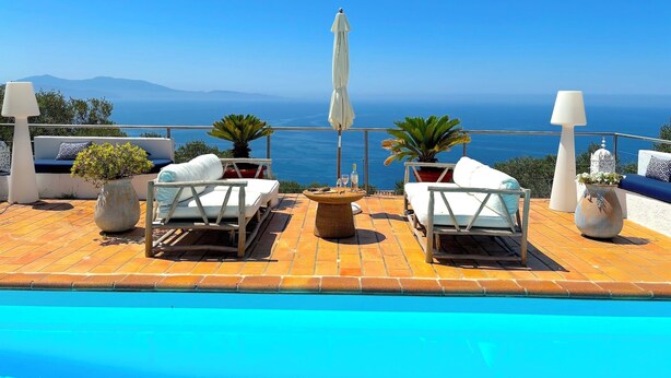 A poolside area with lounge chairs and umbrellas overlooking a clear blue sea and distant mountains. - Villa Paomia (cargèse)