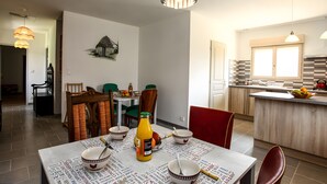 A dining area with a table set for four, a kitchen with a modern design, and a dining chair with a red cushion.