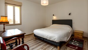 A bedroom with a bed, a desk, a chair, a lamp, a nightstand, and a window.