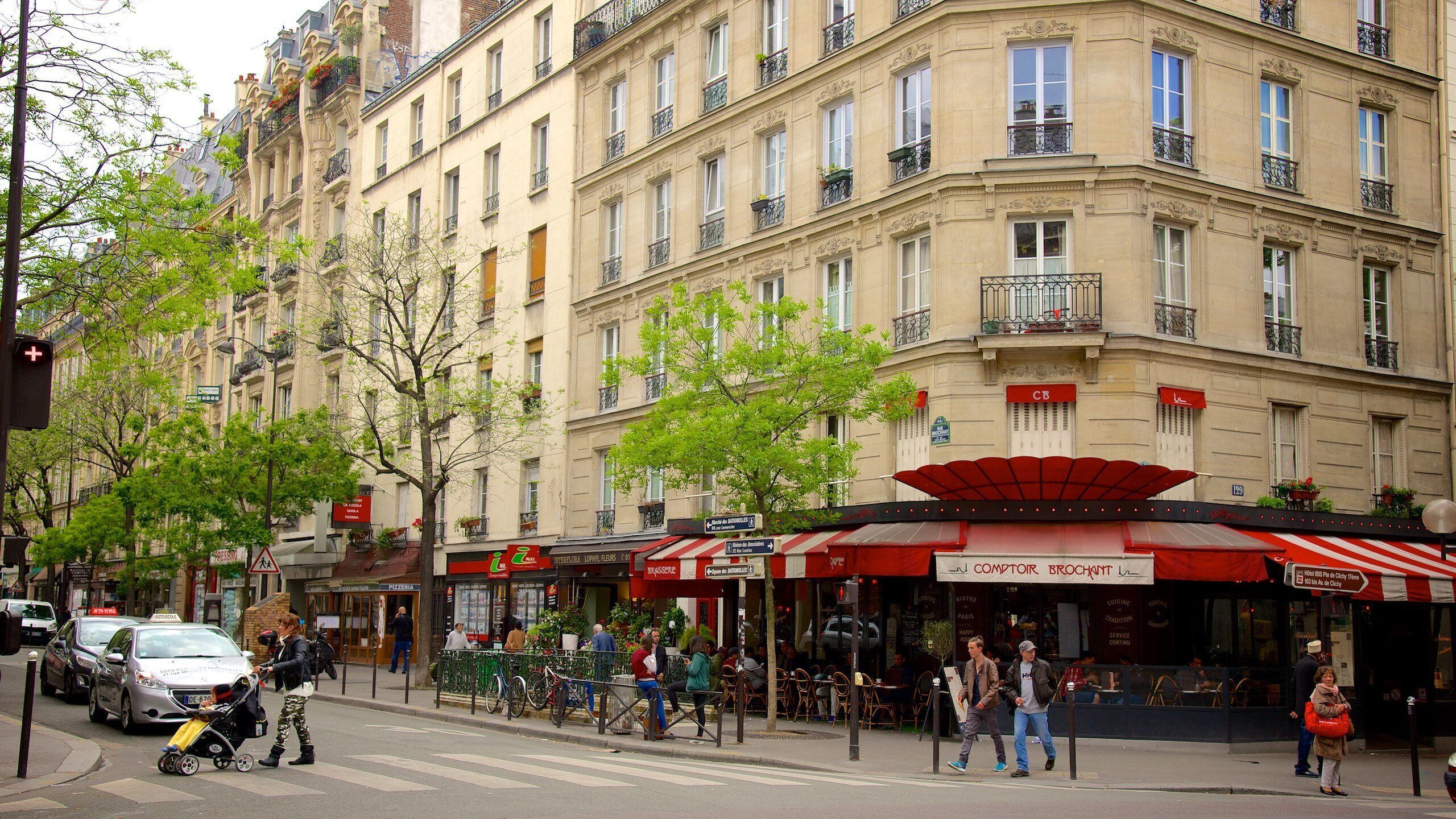 A street view with a cafe named 'COMPTOIR BROCHANT' with outdoor seating, a building with multiple stories, and a crosswalk.