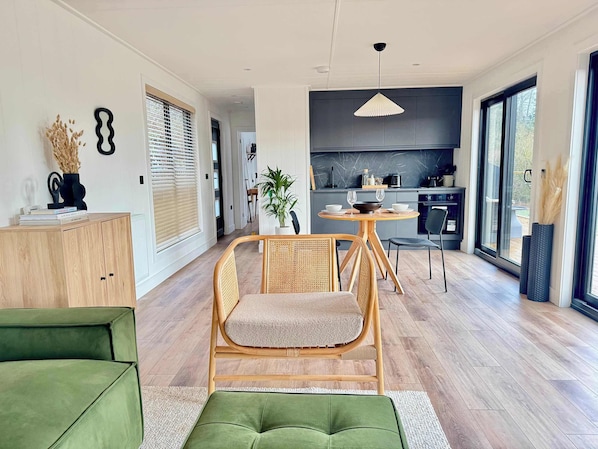 A modern living room with a dining area, a kitchen, and a large window.