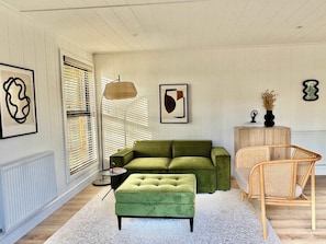 A room with a green sofa, a matching ottoman, a wicker chair, and a floor lamp.