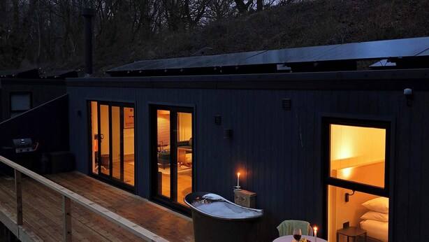 Een moderne cabin met een houten terras, een bubbelbad en een eethoek met een tafel en stoelen.