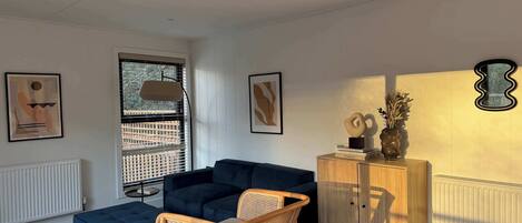 A modern living room with a dark blue sectional sofa, a wicker chair, a wooden cabinet with decorative items, and abstract wall art.