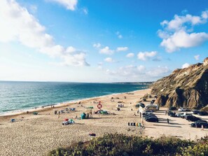 Een strand met een redershutje, parasols en auto's langs de kust.
