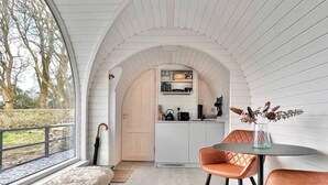 Un intérieur chaleureux avec un banc en bois, une table entourée de chaises et une vue sur la cuisine, accessible par un passage en arc de cercle.