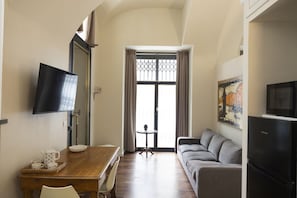 Quarto com uma mesa de jantar de madeira, um sofá, uma TV na parede e uma janela com cortinas.