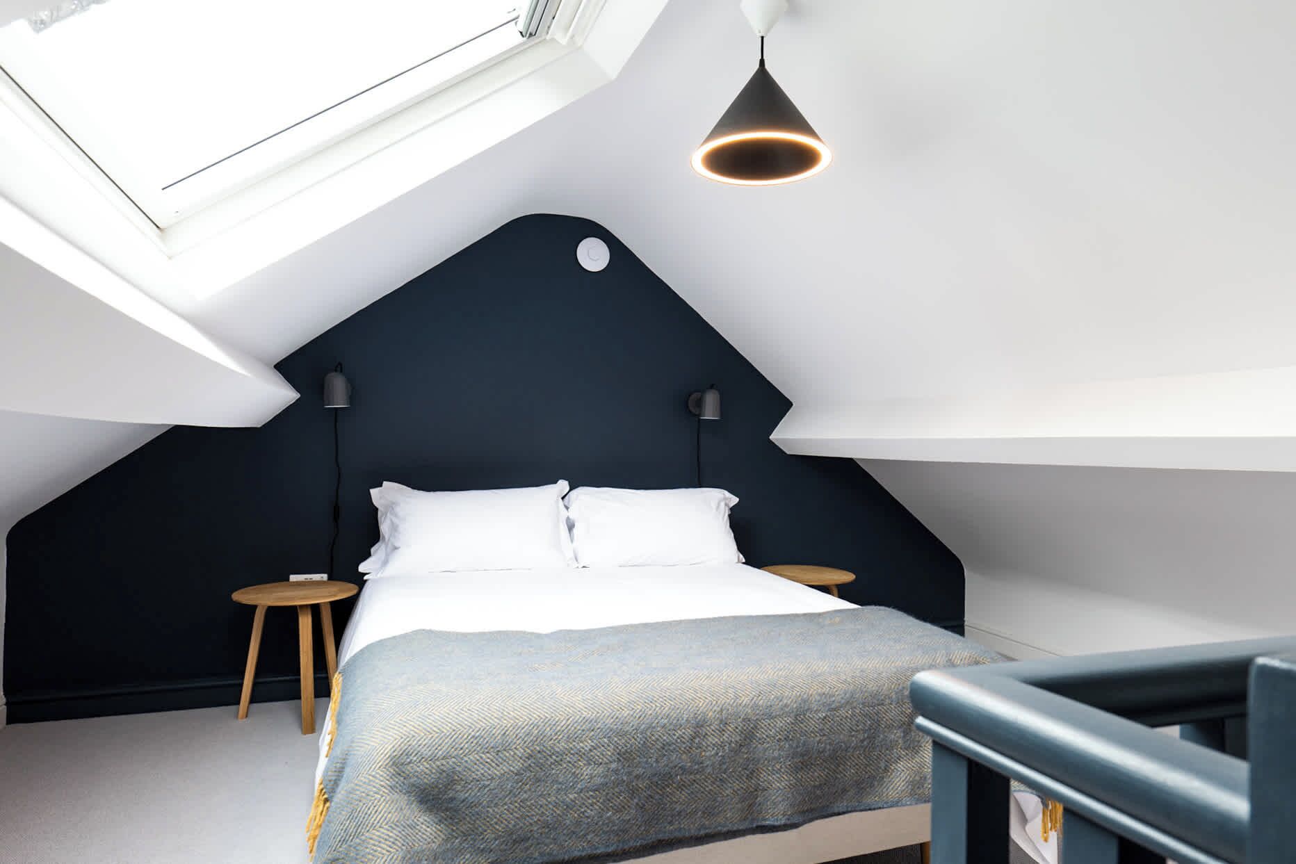 A modern bedroom with a sloped ceiling, a bed with white linens, two bedside tables, and a pendant light.