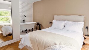 A bedroom with a large bed, a white headboard, a white bathtub, and a mirror.