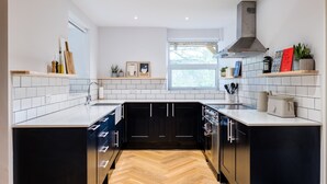 A modern kitchen with white tiles, black cabinets, and a herringbone wood floor.