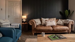 Ett vardagsrum med en brun lädersoffa, en blå fåtölj, ett litet runt bord med en lampa och en kaffekopp på ett träbord.