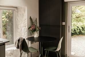 Ein Essbereich mit einem runden Tisch, zwei Stühlen, einer Vase mit Blumen und Blick auf Grünflächen.