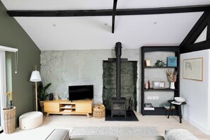 Una sala de estar acogedora con una pared de piedra, un estufa de leña negra, un televisor y una estantería con objetos decorativos.