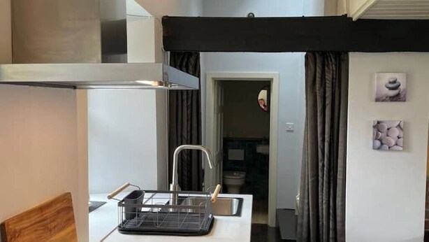 Une cuisine compacte au design moderne, dotée d’un évier en acier inoxydable, d’un plan de travail noir et d’une tête de lit en bois.