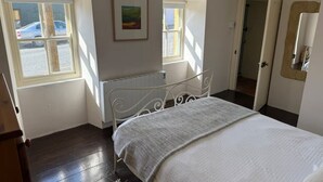 Une chambre à coucher avec un lit, deux fenêtres, un radiateur et une porte.