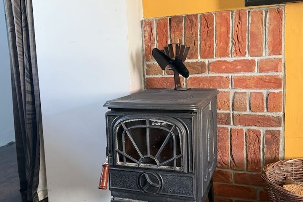 Estufa de madera Stanley antigua con chimenea, frente a un muro de ladrillo y una pared amarilla.