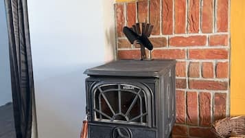 Estufa de madera Stanley antigua con chimenea, frente a un muro de ladrillo y una pared amarilla.