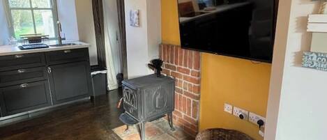 Una cocina con armarios oscuros, una estufa, un televisor montado en la pared y un ventanal.