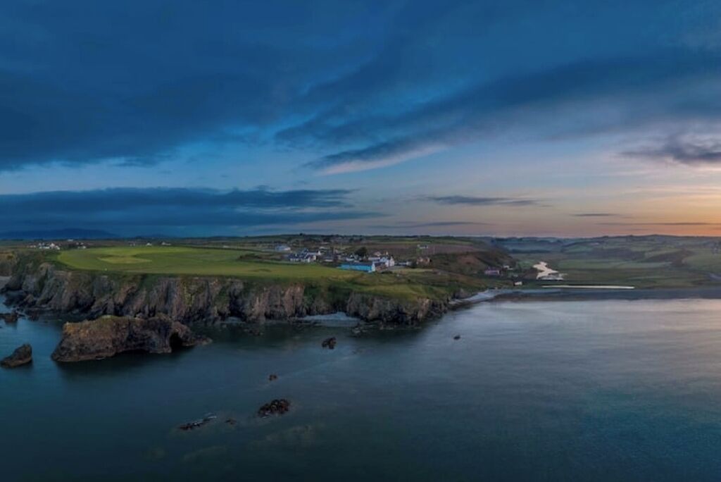 An aerial view of a coastal area with a golf course, a lighthouse, and rocky shores.