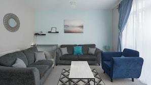 A living room with a grey sofa, a blue armchair, a coffee table, and a wall-mounted mirror.